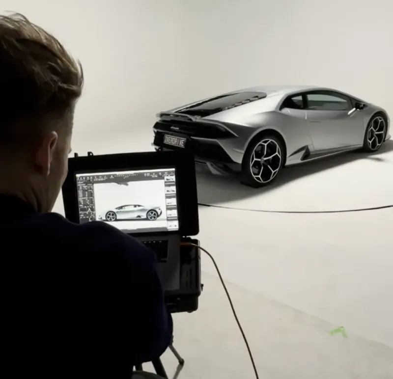 Coulisses d'un shooting automobile : écran de contrôle affichant la voiture de sport sur fond blanc