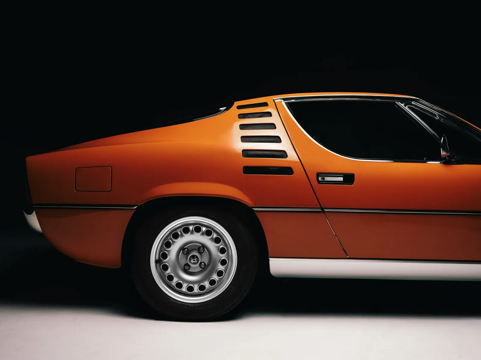 Alfa Romeo Montreal orange de profil sur fond noir : aile arrière, ouïes et jante