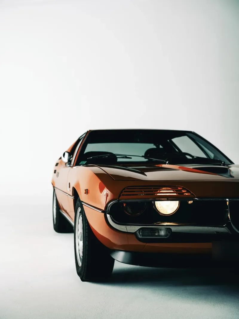 Alfa Romeo Montreal orange, phare allumé, vue de trois quarts avant sur fond blanc